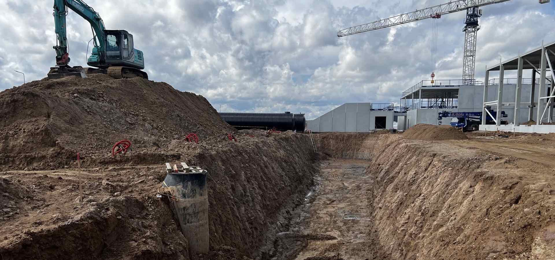 Excavator on a mound of soil above a deep stormwater trench at a building site
