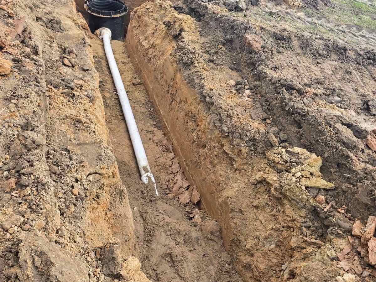 Drenažo vamzdis tranšėjoje veda į plastikinį surinkimo šulinį